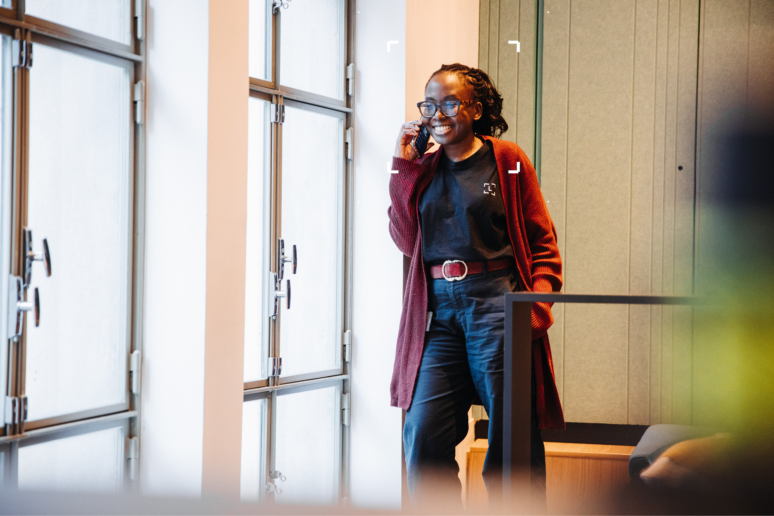 A woman standing next to a window smiling on the phone
