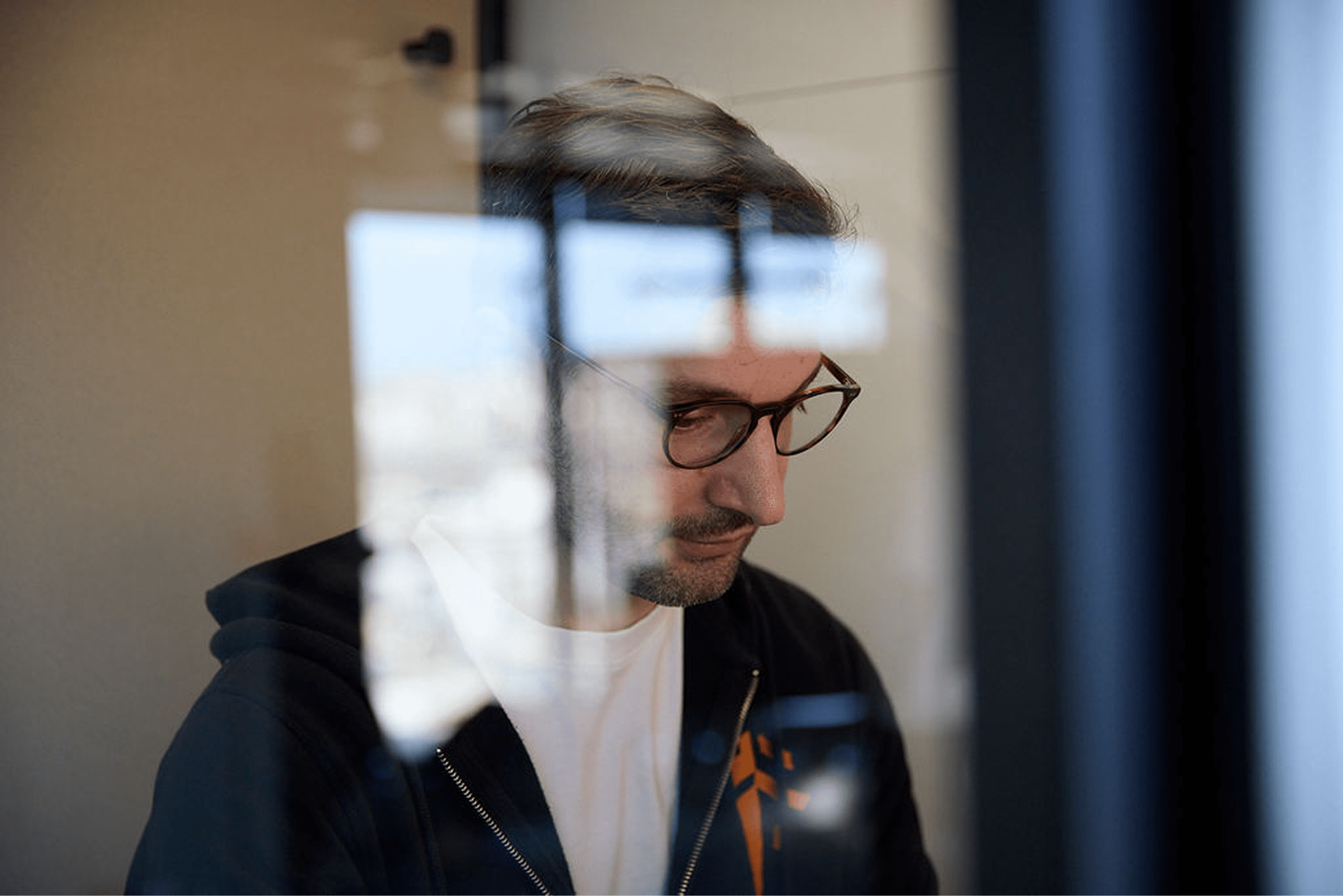 Man sitting in a work pod on his own with a reflective glare across his face